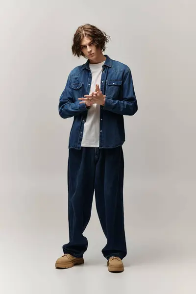 A young, handsome man stands confidently in a trendy denim ensemble, exuding style and charisma. — Stock Photo