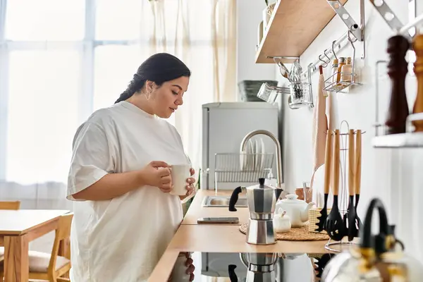 Young woman enjoys a moment of calm in her cozy kitchen, savoring a hot beverage. — Stock Photo