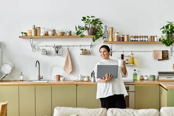 Cozinha brilhante repleta de plantas onde uma mulher bonita e de tamanho grande tem feliz um laptop e xícara. — Fotografia de Stock