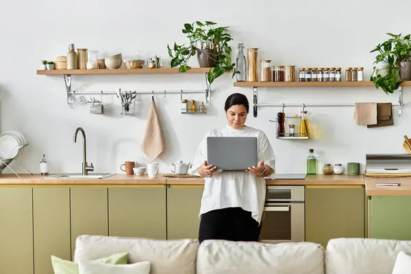 Uma cozinha brilhante onde uma mulher bonita plus size usa seu laptop. — Fotografia de Stock