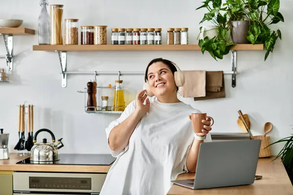 A young plus sized woman smiles while holding a warm drink in her stylish kitchen, enjoying her day. — Stock Photo