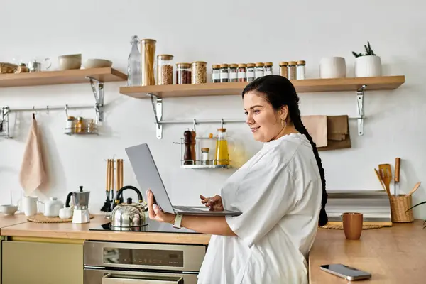 Bright and inviting kitchen filled with warmth as a woman engages with her laptop, smiling. — Stock Photo