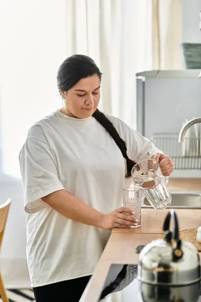 A young plus sized woman pours water into a glass, savoring a moment in her kitchen. — Stock Photo