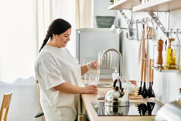 Joy llena la cocina mientras una joven y hermosa mujer vierte agua en un vaso, irradiando felicidad. - foto de stock
