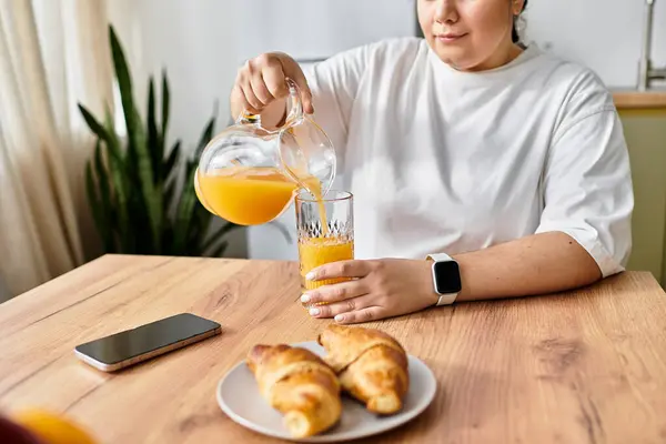 A young woman enjoys a delightful breakfast, pouring orange juice while sitting at a cozy table. — Stock Photo