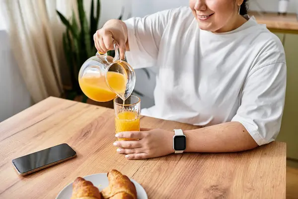 Pouring fresh orange juice into a glass while enjoying a delicious breakfast at home — Stock Photo