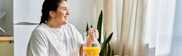 Bright sunlight filters through the window as a young plus sized woman smiles while pouring juice. — Stock Photo