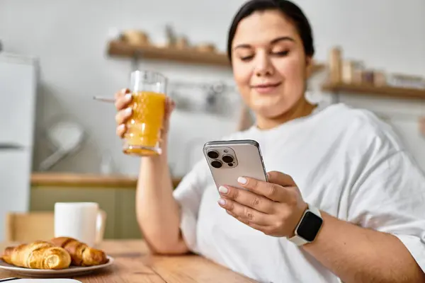 A young plus sized woman relaxes at a rustic cafe, sipping a drink and scrolling on her smartphone. — Stock Photo