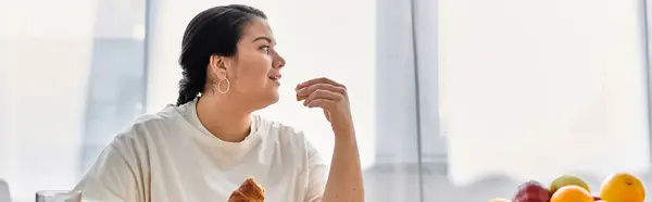 A young plus size woman sits thoughtfully, savoring a tasty treat in a bright and airy space. — Stock Photo