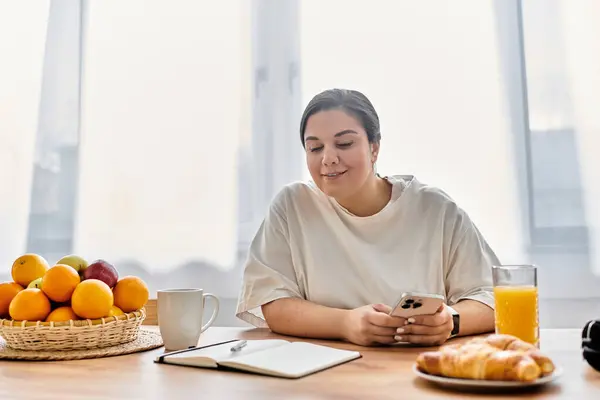 Bright sunlight floods the kitchen as a young plus sized woman enjoys breakfast with a smile. — Stock Photo