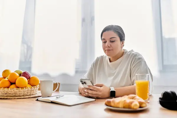 A young plus sized woman checks her phone over breakfast in a bright morning ambiance. — Stock Photo