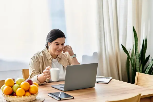 A young beautiful plus sized woman smiles as she sips a warm drink while working at her table — Stock Photo