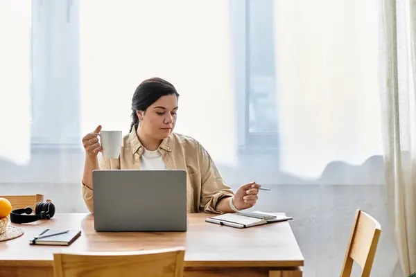 Una giovane donna plus size sorseggia caffè mentre lavora sul suo computer portatile in un luminoso home office. — Foto stock