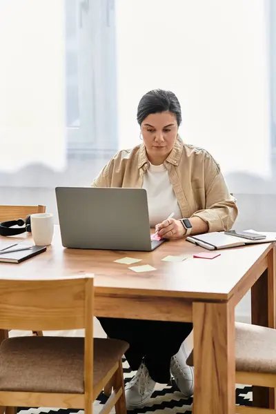 Focused young woman engages with her laptop at a cozy workspace filled with natural light. — Stock Photo
