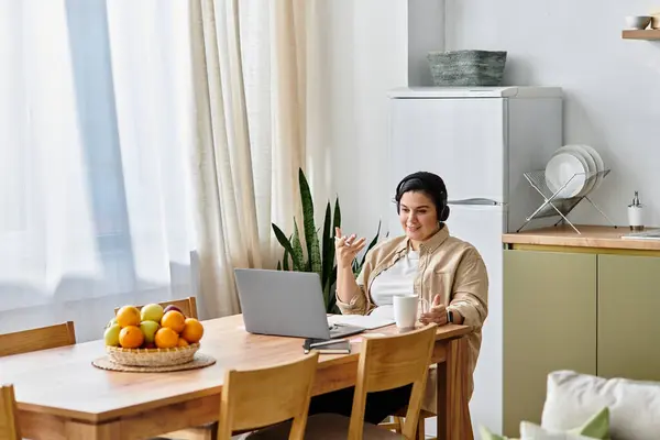 A beautiful young plus sized woman enjoys a lively virtual chat while seated at her dining table. — Stock Photo
