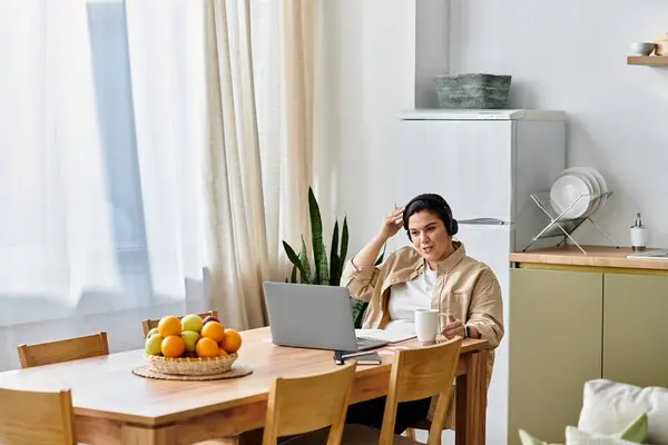 Una giovane donna plus size si siede a un tavolo in una cucina soleggiata, godendo il suo lavoro caffè e laptop. — Foto stock