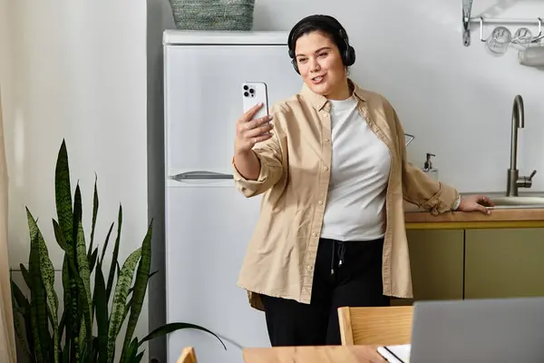 A young plus sized woman smiles for a selfie in her modern kitchen, savoring the moment. — Stock Photo