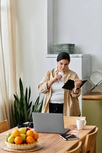 Young plus sized woman thoughtfully reviews her notes, sipping a drink in a cozy kitchen setting. — Stock Photo