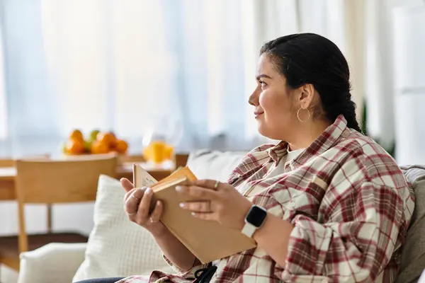 A young plus sized woman enjoys reading in a bright living room filled with natural light. — Stock Photo