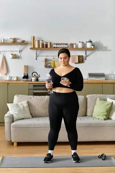 A young plus sized woman in her home gym gets ready for a workout with a water bottle. — Stock Photo