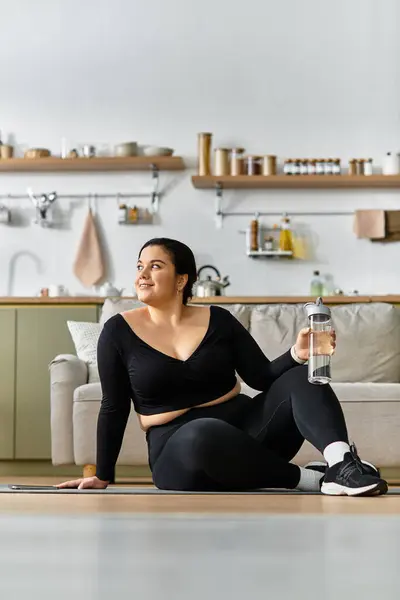 In a cozy home, a young plus sized woman relaxes with a water bottle after exercising on the floor. — Stock Photo