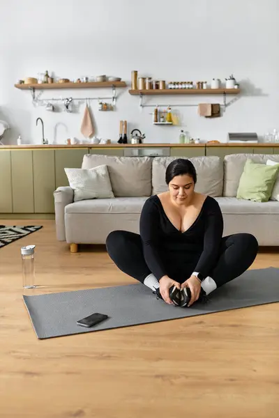 Молодая женщина плюс размер растягивает на циновке yoga в стильной гостиной, упором на wellness. — стоковое фото