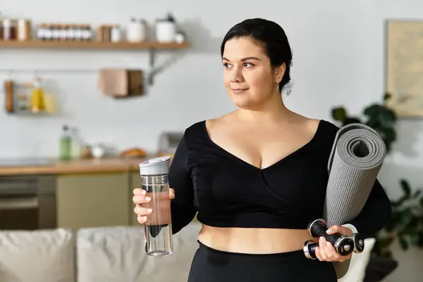 Уверенная в себе женщина plus-size держит в яркой комнате носки и бутылку с водой, готовая к тренировкам. — стоковое фото