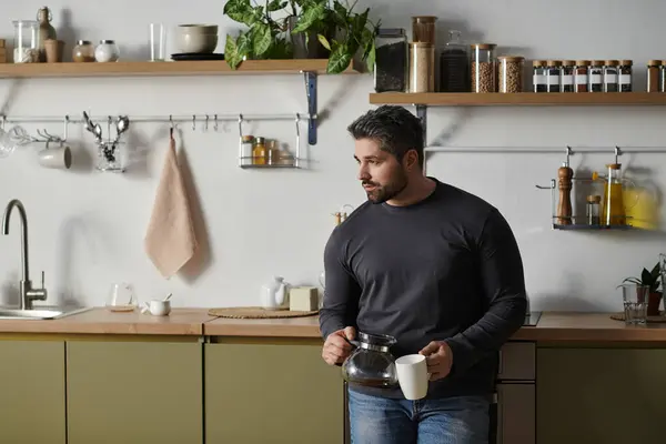 A handsome man pours coffee in his stylish kitchen, surrounded by greenery. — Stock Photo