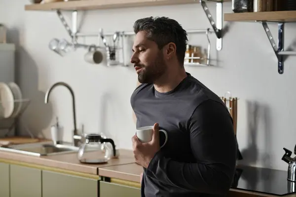 Un homme élégant prend une pause, tenant une tasse de café tout perdu dans la pensée à sa cuisine chic. — Photo de stock