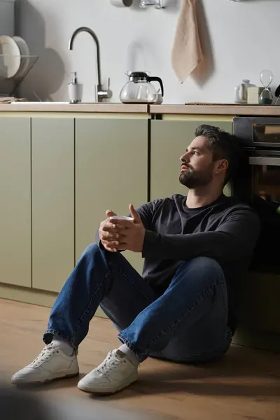 A handsome man sits on the kitchen floor, reflecting in the serene afternoon light. — Stock Photo