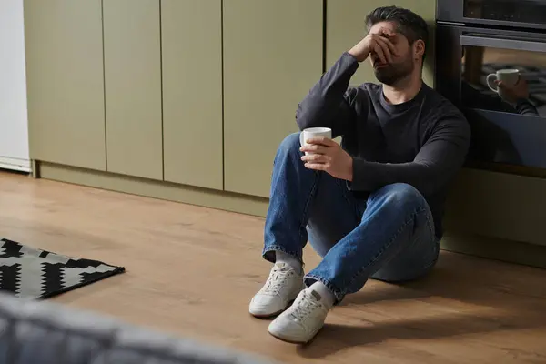 A man appears contemplative while seated on the floor, holding a cup in a stylish interior. — Stock Photo