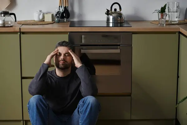 A handsome man sits on the kitchen floor, hands resting on his head, embracing tranquility. — Stock Photo