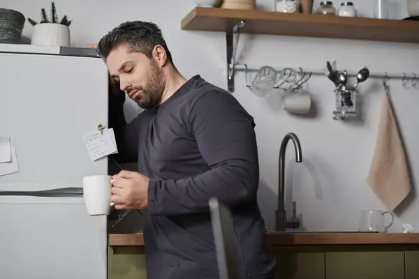 Un hombre guapo vierte café en una taza, saboreando una mañana tranquila en su elegante cocina. - foto de stock