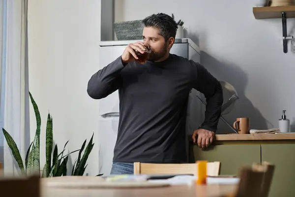 In a relaxed moment, a handsome man savors his drink while leaning against the kitchen counter. — Stock Photo