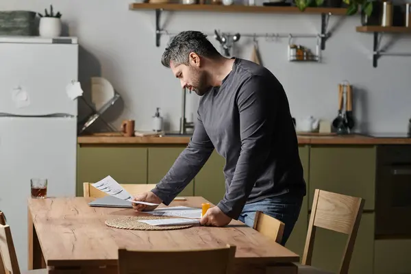 A man studies important papers at a chic kitchen table in the afternoon light. — Stock Photo