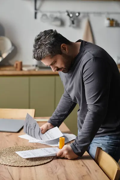 A handsome man carefully examines paperwork while standing at a modern kitchen table. — Stock Photo