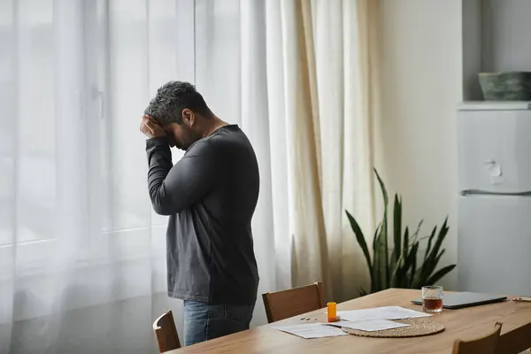 Un homme réfléchi se penche contre une fenêtre, contemplant des difficultés de vie dans une cuisine sereine. — Photo de stock