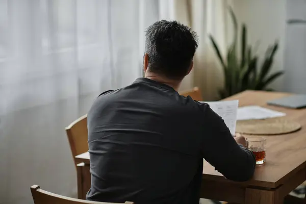A man thoughtfully sips a drink and studies notes at a wooden table in a cozy space. — Stock Photo