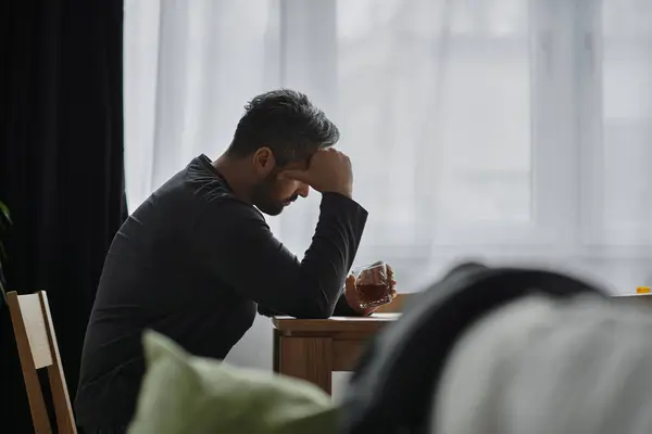A handsome man sits at a table in deep thought, holding a glass, lost in reflection. — Stock Photo