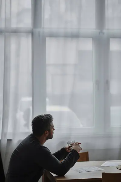 A thoughtful man gazes out the window while sipping a warm beverage in an intimate setting. — Stock Photo