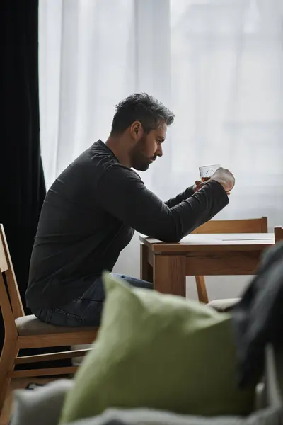 A handsome man sits thoughtfully at a wooden table, savoring his drink in a serene space. — Stock Photo