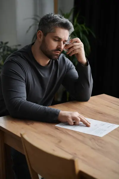 A handsome man sits at a wooden table, thoughtfully reviewing important documents. — Stock Photo