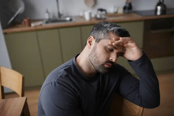Um homem bonito descansa a testa em sua mão, perdido em pensamento em uma cozinha elegante. — Fotografia de Stock