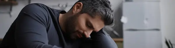 A handsome man sits quietly, lost in thought, in a warm and inviting indoor environment. — Stock Photo