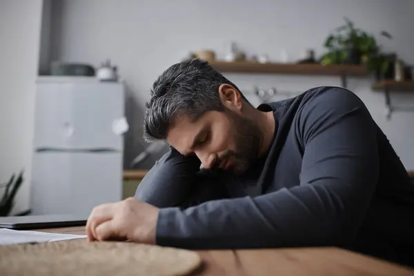 A handsome man with dark hair leans on a wooden table, reflecting in a warm, inviting room. — Stock Photo
