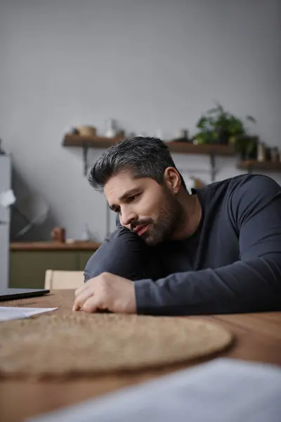 Un homme avec une belle apparence est assis à une table en bois, profondément dans la pensée tout en examinant la paperasserie. — Photo de stock