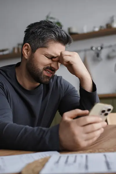 Un bell'uomo si siede a un tavolo di legno, sentendosi stressato mentre controlla il telefono in uno spazio caldo. — Foto stock