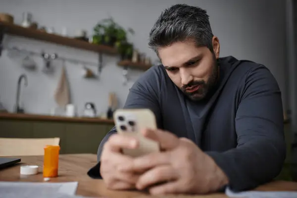 Ein gutaussehender Mann sitzt mit seinem Smartphone an einem Holztisch. — Stockfoto