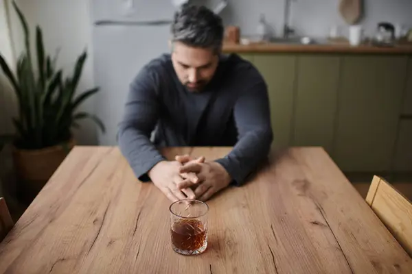 A thoughtful man sits at a wooden table, reflecting quietly on life with a drink in front of him. — Stockfoto