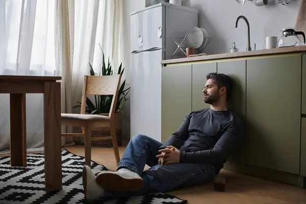 Um homem bonito senta-se no chão da cozinha, profundamente em pensamento em uma atmosfera serena. — Stock Photo